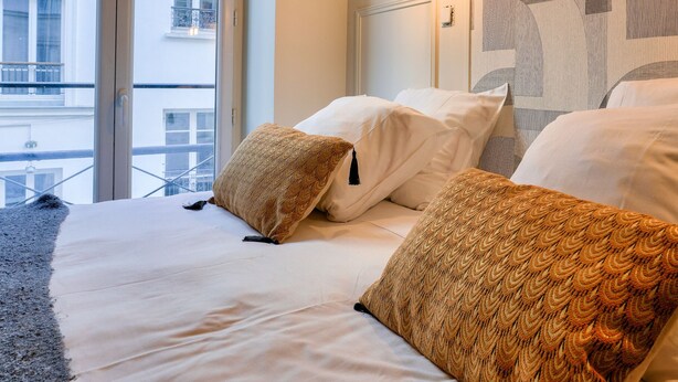 A hotel room with a large bed, two pillows, a wall-mounted light, and a view of a building through a window.