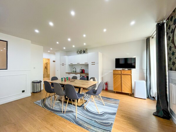 Une cuisine moderne avec des meubles blancs, une table à manger avec des chaises, un téléviseur à écran plat et un tapis à motifs.