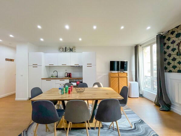 A modern kitchen with white cabinets, a wooden dining table, and a television on a wooden cabinet. - UrbanFlat 17 - Pretty 3 Bedroom Flat in Paris Center (París)