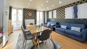 A modern living room with a dining table, sofas, and a large window.