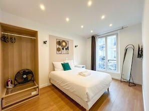 A bedroom with a bed, a fan, a window with a view, and a standing mirror. - UrbanFlat 18 -  Apartment Paris Montorgueil (París)