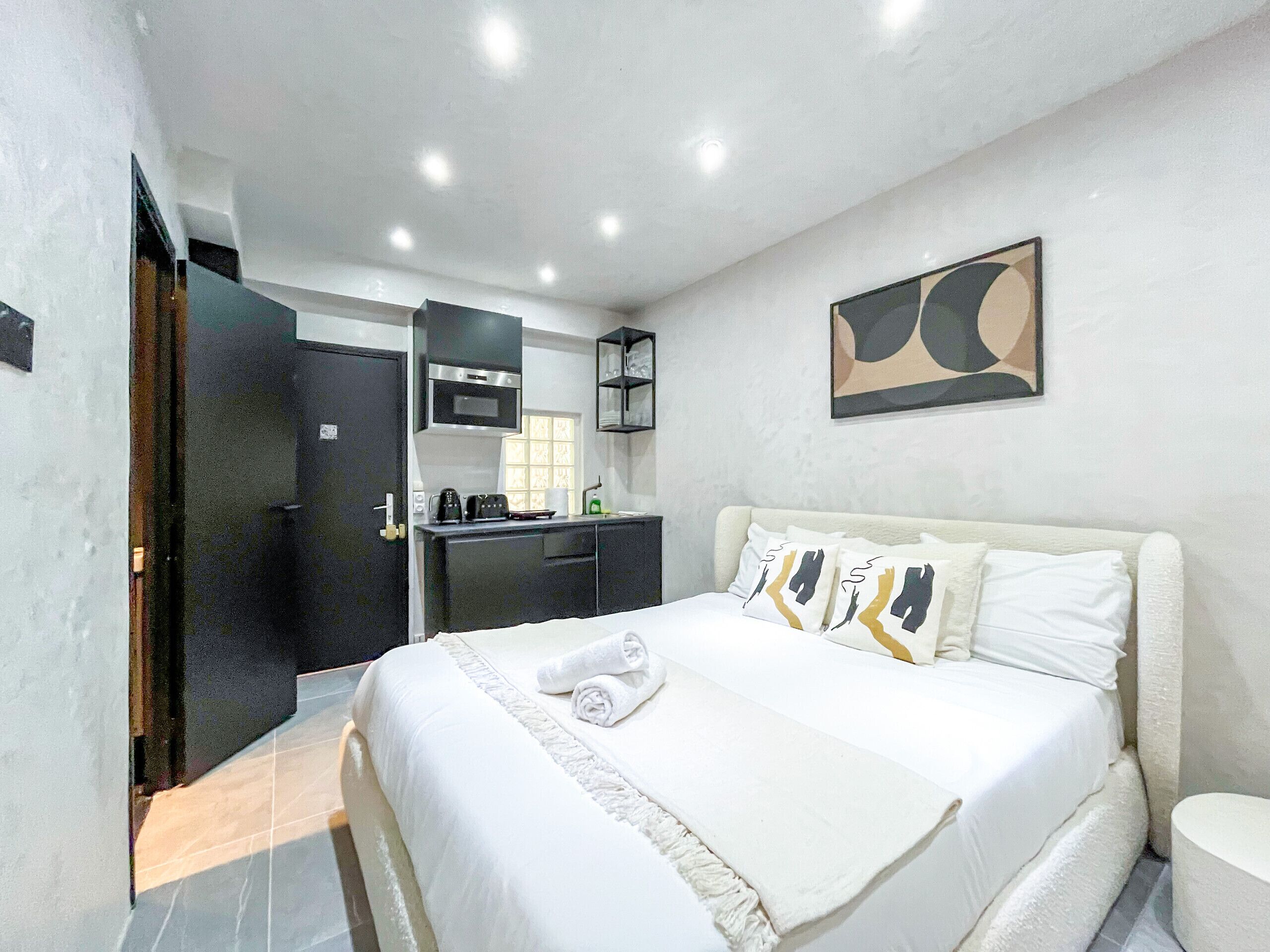 A hotel room with a bed, a bedside table, a small desk with a chair, a microwave, and a window.