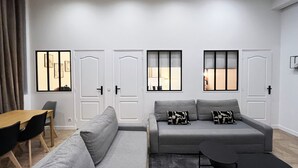 A modern living room with a grey sofa, a small table, and chairs. There are three doors with windows, and a curtain is partially visible. - Urban Flat 66 - Pretty 3 bedroom in Paris (París)