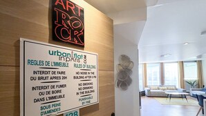 Un letrero que enumera las normas del edificio en francés e inglés, una obra de arte de neón y una sala de estar moderna con un sofá y una mesa de centro.