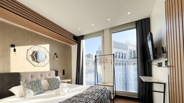 Una habitación de hotel moderna con una cama grande, un espejo, un televisor y vistas a la ciudad.