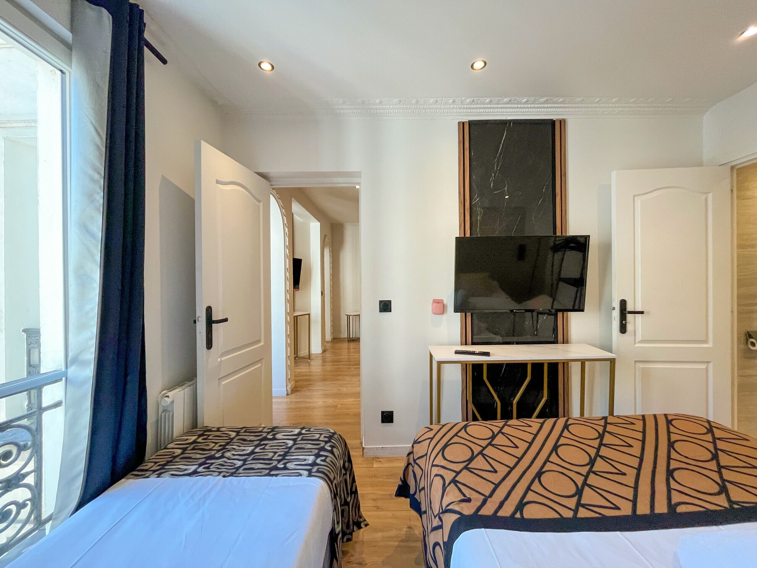 A hotel room with two beds, a TV on a stand, a desk, and a view of the hallway.