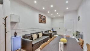 A modern living room with a long dining table, sofas, and a small cabinet.