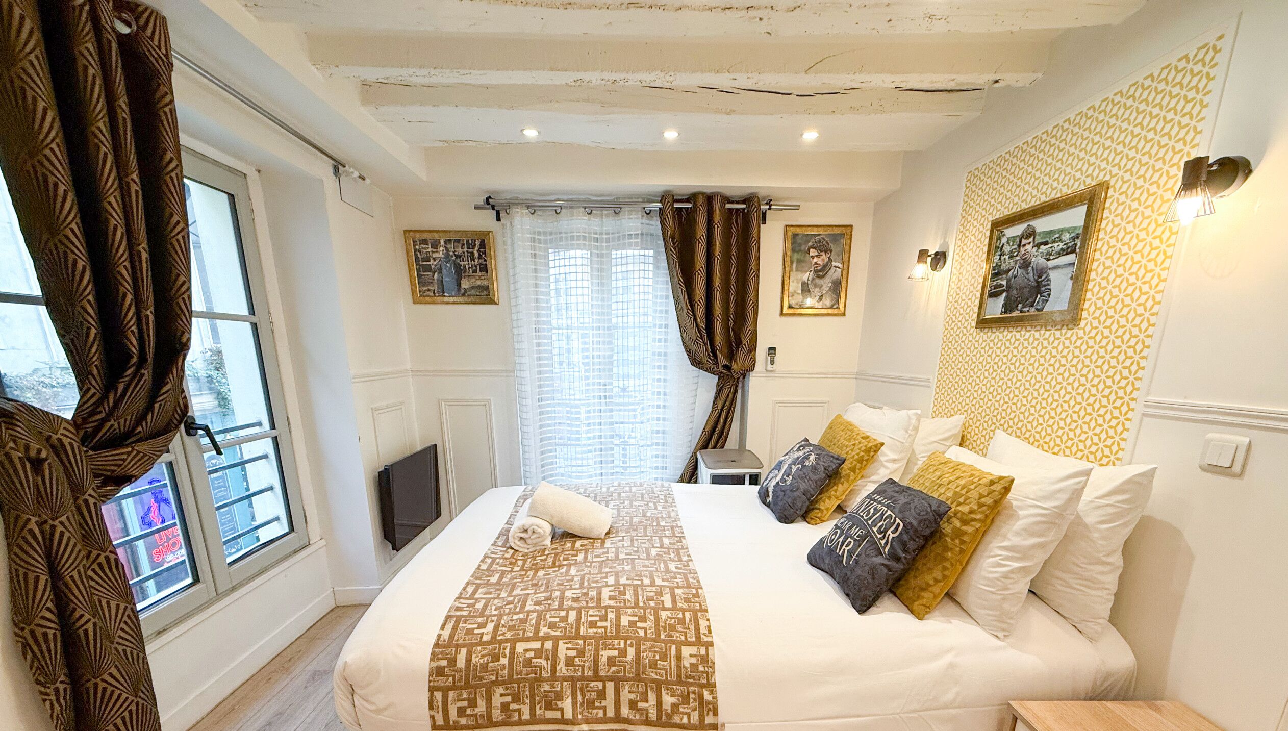 A hotel room with a bed, curtains, a window, and wall-mounted pictures.