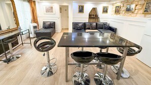 Ein modernes Wohnzimmer mit einem schwarzen Sofa, einem Esstisch mit Barhocker, einem großen Spiegel und einer Steinwand mit gerahmten Bildern.