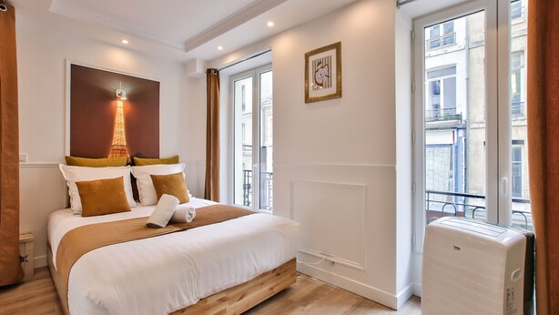 Una habitación de hotel con cama, radiador y ventana con vistas a edificios.