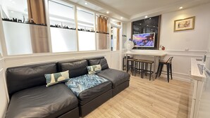 Una sala de estar moderna con un sofá de cuero negro, un televisor y vistas a un paisaje urbano.