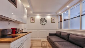 Una cocina moderna con encimera de madera, una cafetera roja y un horno empotrado. En la zona de estar, hay un adorno circular en la pared y un sofá de cuero marrón.
