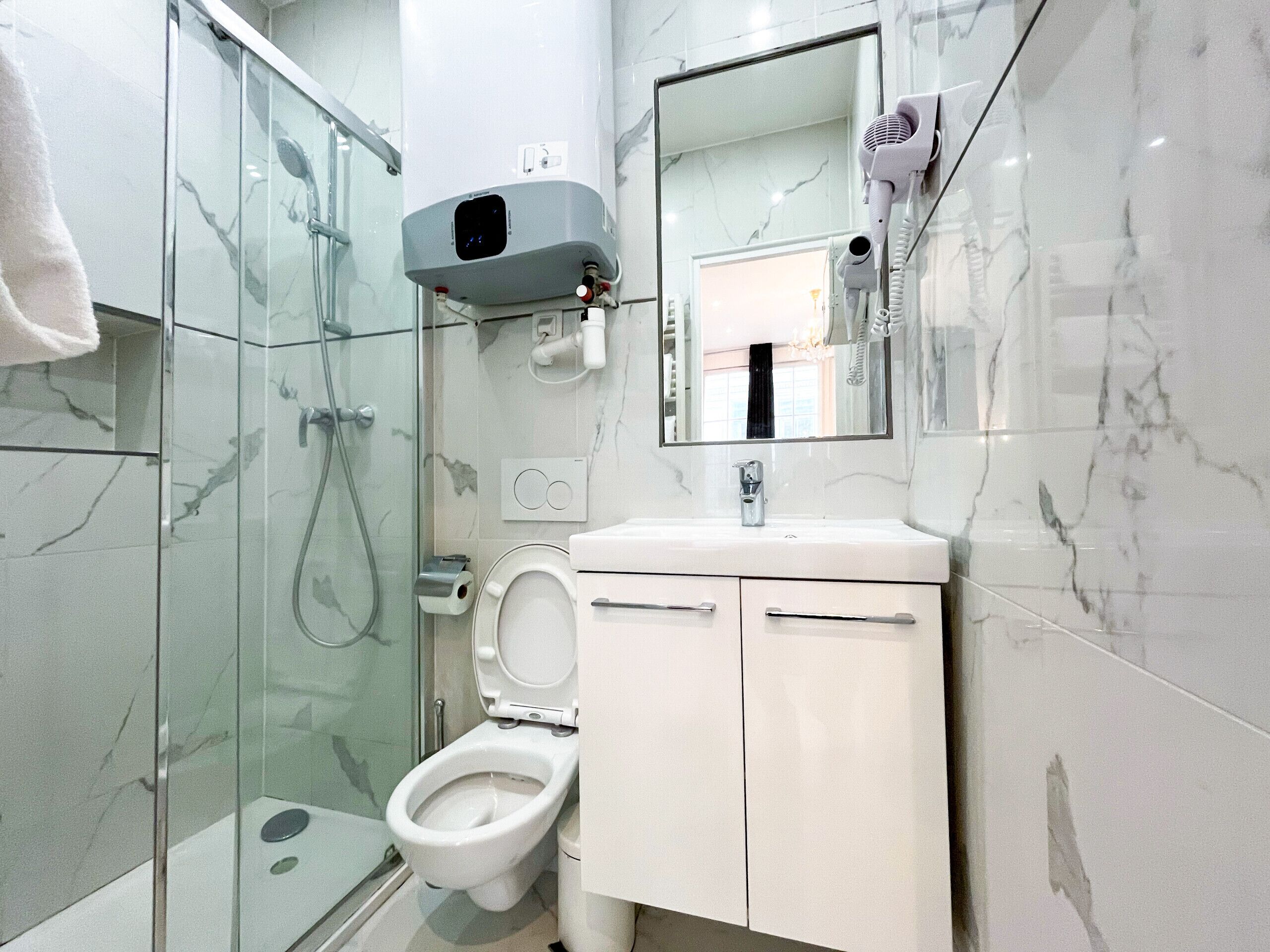 A modern bathroom with a glass shower enclosure, a toilet, a sink with a mirror above it, and a hairdryer mounted on the wall.