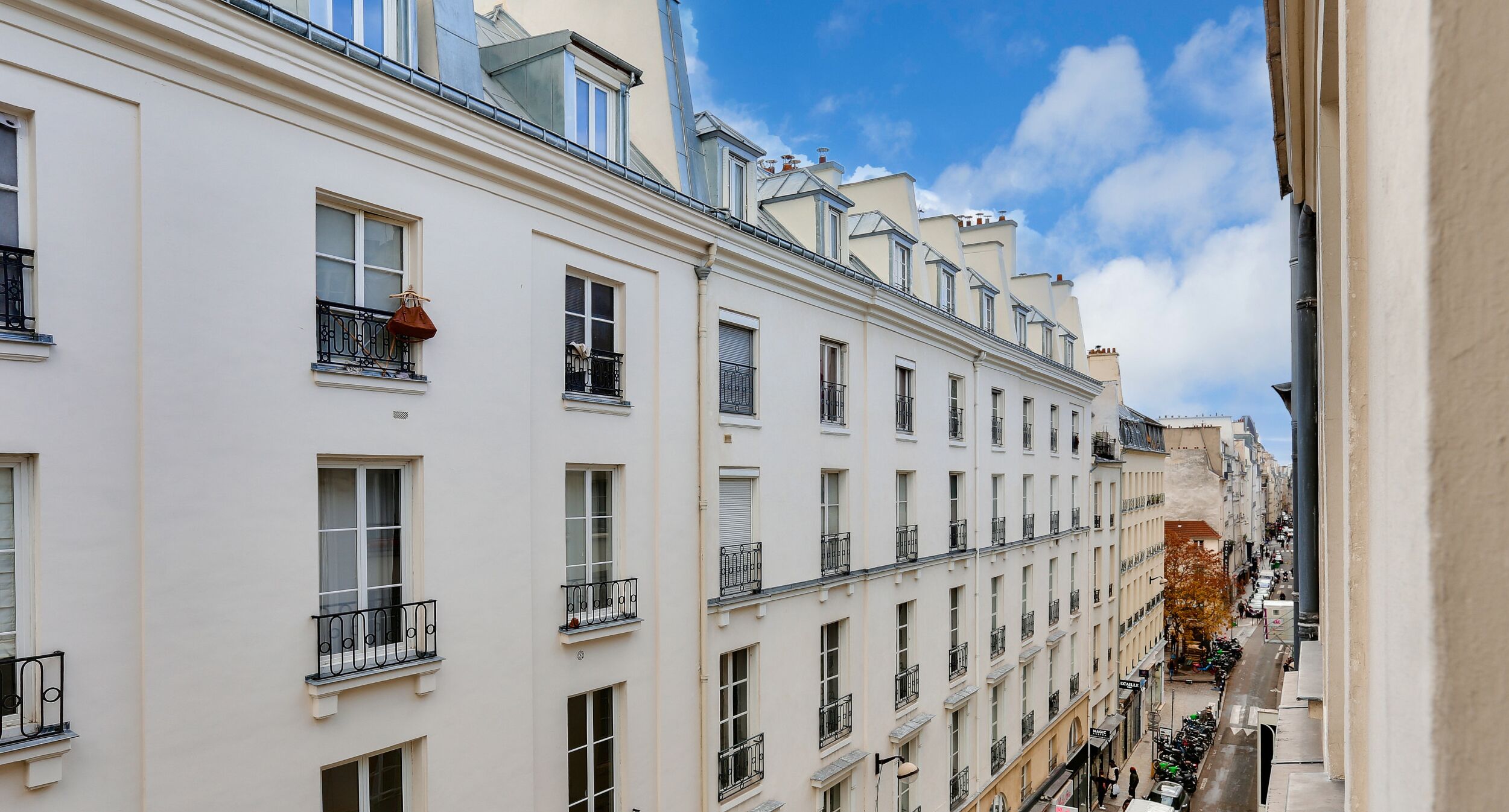 A row of white buildings with balconies and windows, a clear sky, and a narrow street below.