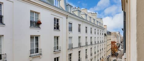 A row of white buildings with balconies and windows, a clear sky, and a narrow street below.