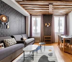 Een moderne woonkamer met een grijze bank, een klein rond tafeltje en een eethoek met een houten tafel en stoelen.