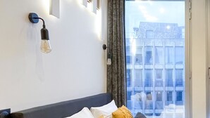 A hotel room with a bed, a wall-mounted light fixture, a window with curtains, and a view of buildings outside. - Urban Flat 129 - Art Love Champs-Elys&eacute;es (París)