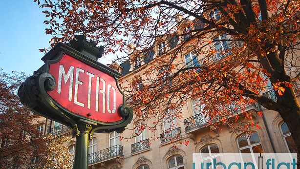 A red 'METRO' sign with ornate metalwork, set against a backdrop of a historic building with balconies and arched windows, surrounded by autumn foliage. - Urban Flat 129 - Art Love Champs-Elys&eacute;es (París)