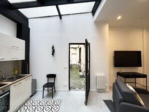 A modern kitchen with a dining area, a TV, and a view through an open door to a courtyard.