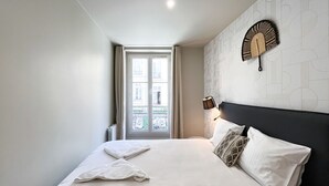 Een slaapkamer met een groot bed, een raam met gordijnen, een wandlamp en een behang met patroon.