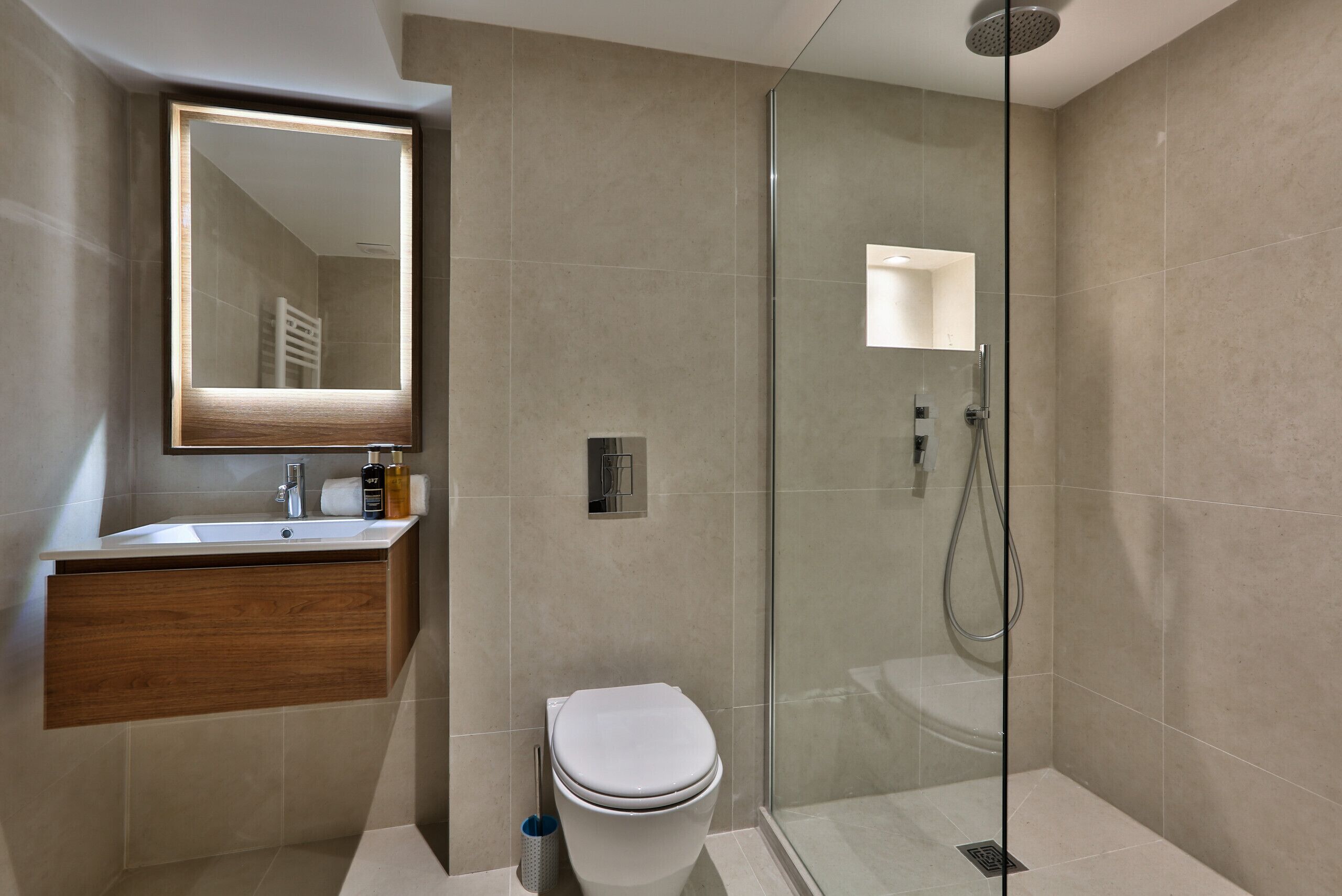 Een moderne badkamer met een douchecabine van glas, een houten wastafelmeubel en een grote spiegel.