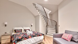 A bedroom with a bed, a sofa, a staircase, and a nightstand.