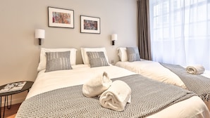 A hotel room with two beds, a small table, and two wall-mounted lamps.