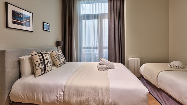 Habitación de hotel con una cama grande, dos camas más pequeñas, un radiador y una ventana con cortinas.