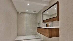 Un baño moderno con ducha envuelta en vidrio, tocador de madera y un espejo grande.