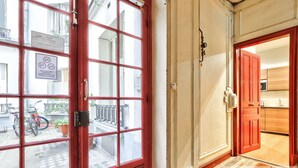 A red-framed door with a view of a bicycle and plants outside, leading to a kitchen area with wooden cabinets. - Urban Flat  140 - Beautiful Flat near Saint-Germain des Pres (París)