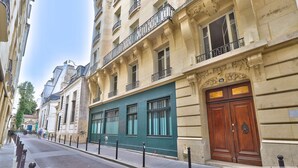 A street view with a building featuring a green facade, a wooden door, and a balcony with black railings. - Urban Flat  140 - Beautiful Flat near Saint-Germain des Pres (París)