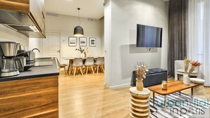 A modern kitchen with a coffee maker, dining area with chairs, a TV mounted on the wall, and a seating area with a coffee table and decorative items. - Urban Flat  140 - Beautiful Flat near Saint-Germain des Pres (París)