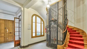 A grand hallway with a wooden door, a large arched window, and a red carpeted staircase. - Urban Flat  140 - Beautiful Flat near Saint-Germain des Pres (París)