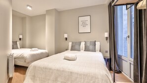 Une chambre d’hôtel avec deux lits, une grande fenêtre avec des rideaux, un lampadaire fixé au mur et une affiche inspirante.
