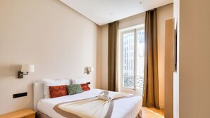 Ein Hotelzimmer mit einem Bett, zwei Wandleuchten, einem Fenster mit Vorhängen und Blick auf Gebäude.