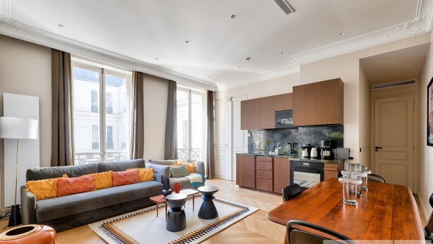 Eine moderne Wohnung mit Wohnzimmer, Essbereich und Küche, ausgestattet mit großen Fenstern und Blick auf die Stadt.