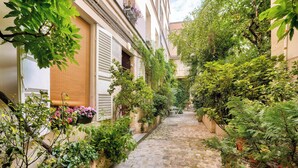 A narrow cobblestone alley flanked by lush greenery and buildings with shutters. - Urban Flat 127 -  4 Bedroom Apartment Paris Montorgueil (París)