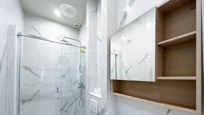 A modern bathroom with a glass-enclosed shower, marble walls, and a wooden shelf unit. - UrbanFlat 64 - Urban Luxury Flat near Champs-Elysées (París)