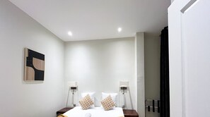 Una habitación de hotel con una cama, lámparas de noche, una obra de arte en la pared y una puerta.