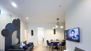 Una sala moderna con un sofá, sillas, un televisor y una mesa de comedor.