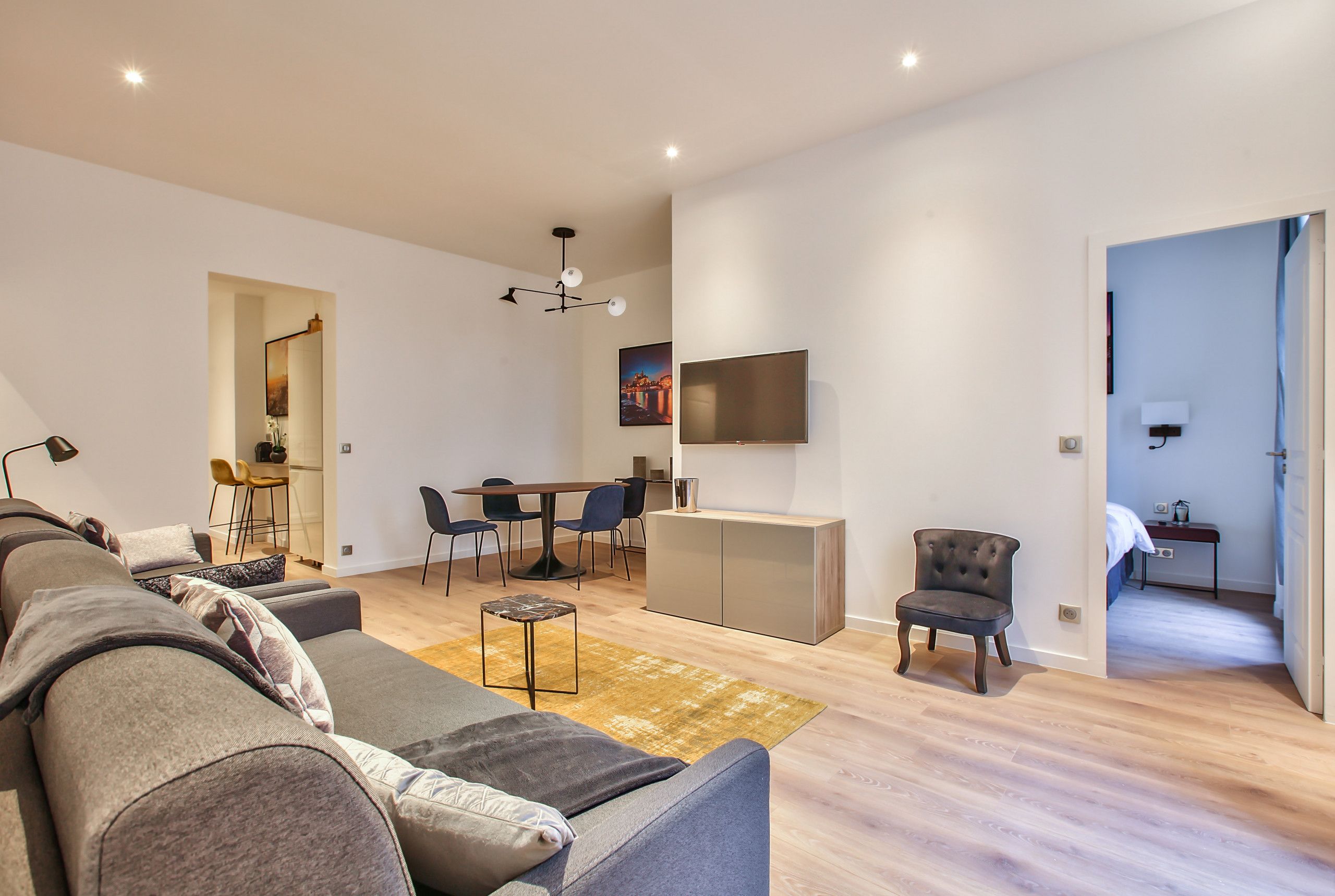Ein modernes Wohnzimmer mit einer Couch, einem Esstisch und einem an der Wand befestigten Fernseher.