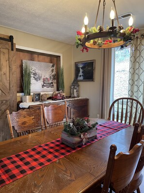 Un coin repas avec une table en bois, des chaises, un lustre et des décorations de fêtes.