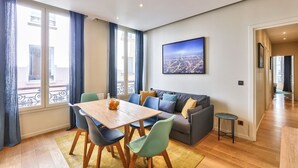 A modern living room with a wooden dining table, colorful chairs, a grey sofa, and a cityscape painting on the wall. - 71 - Urban Amazing Apartment in Le Marais (París)