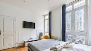 Una camera da letto con un letto, una scrivania, una sedia, una TV e ampie finestre.