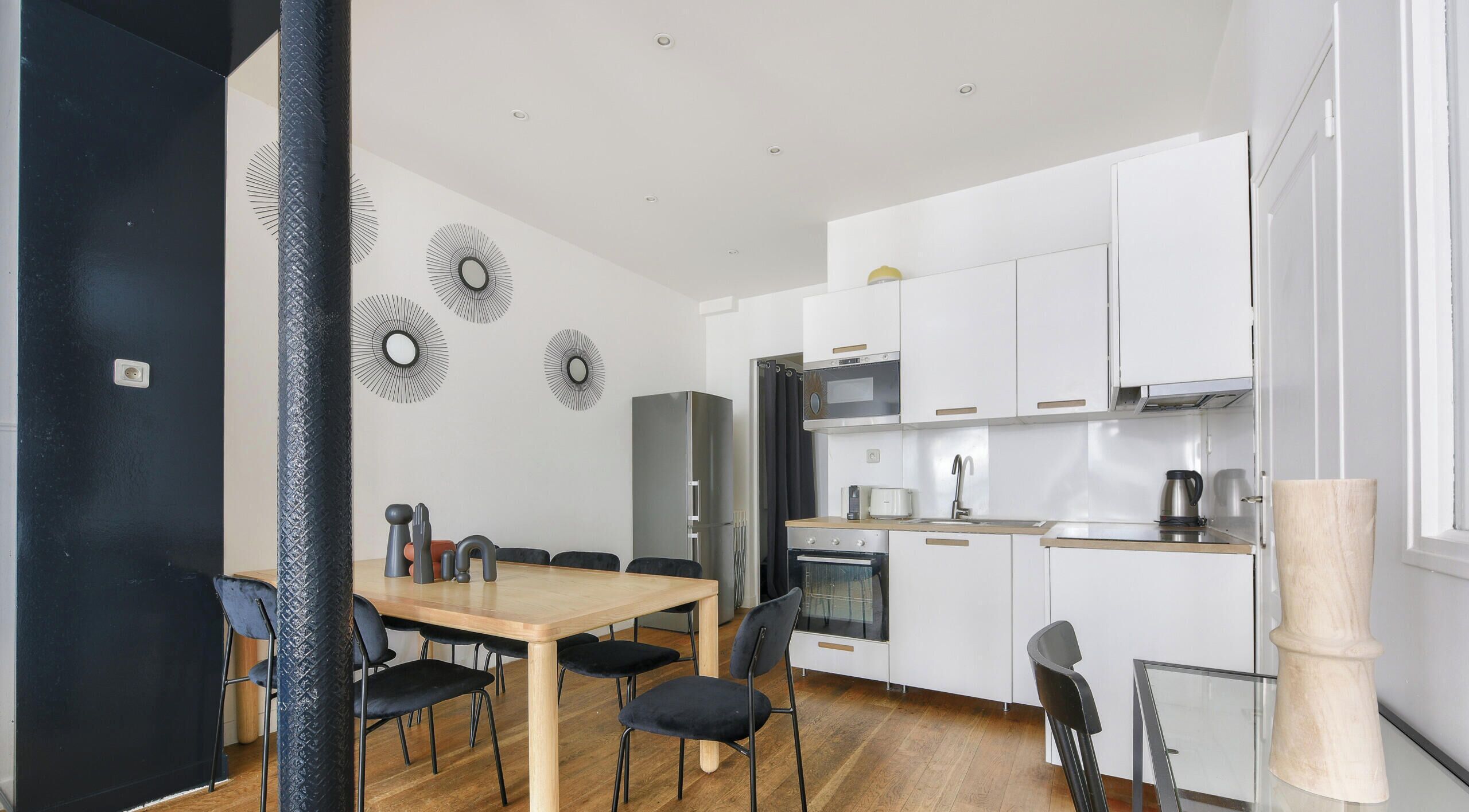 Una cocina moderna con armarios blancos, una mesa de comedor de madera y sillas negras.