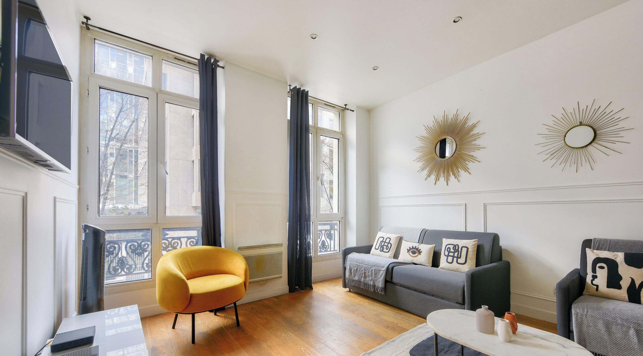 A modern living room with a yellow armchair, grey sofa, and decorative pillows.