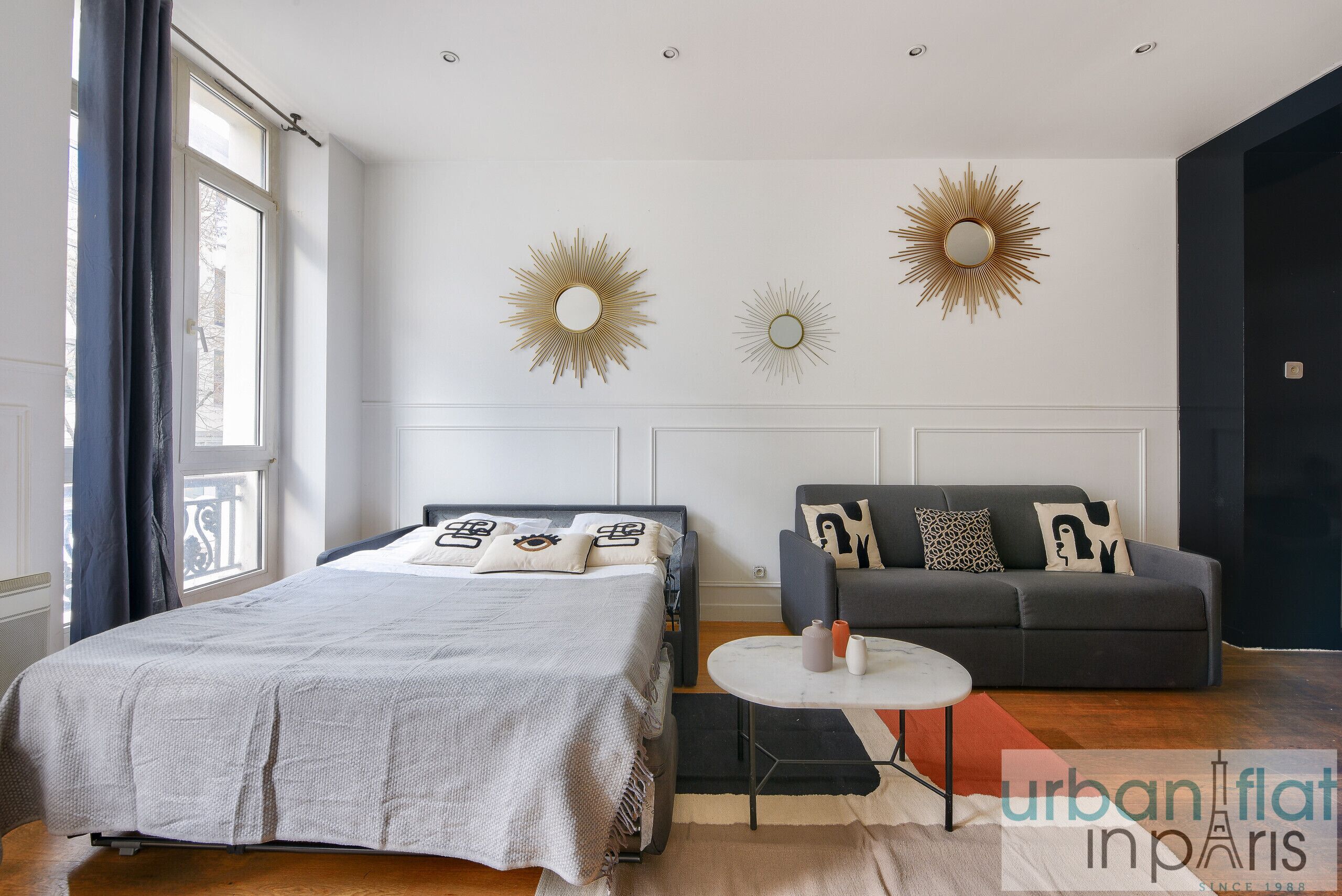 A modern bedroom with a bed, a sofa, and two wall-mounted sunburst mirrors.