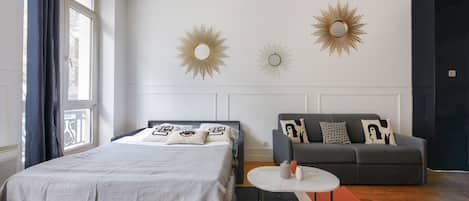 A modern bedroom with a bed, a sofa, and two wall-mounted sunburst mirrors.