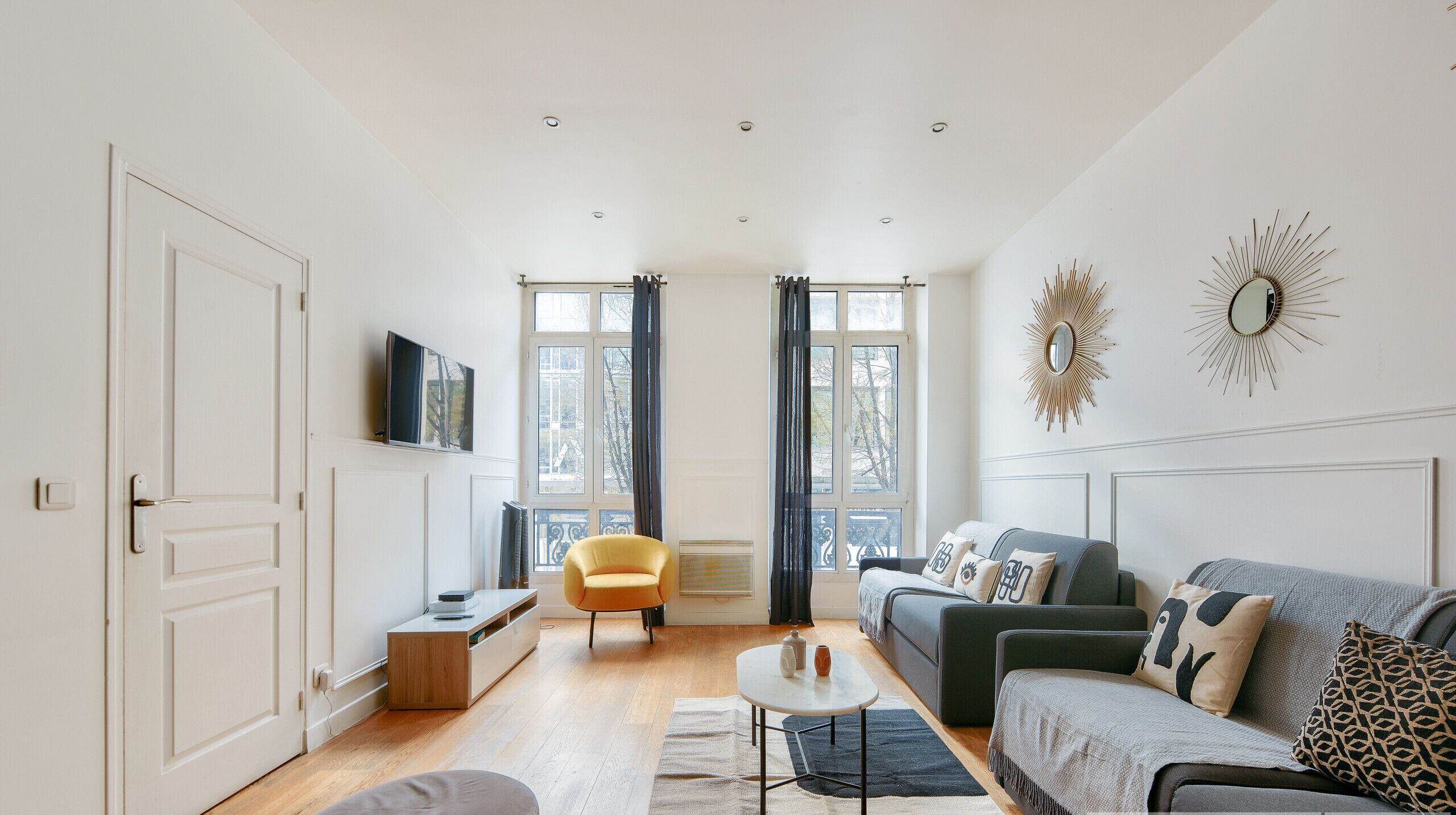 A modern living room with a sofa, a small table, a chair, and a TV on the wall.