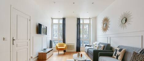 Un salon moderne avec un canapé, une petite table, un fauteuil et un téléviseur fixé au mur.